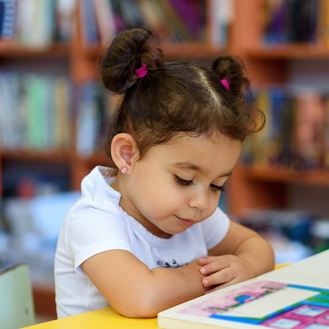 Little girl sitting at table reading a book