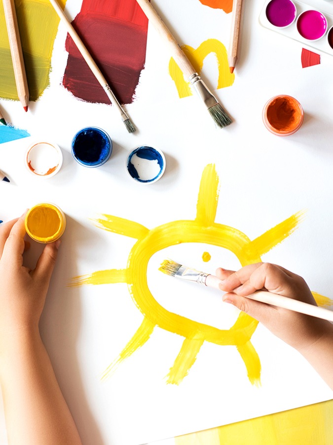 Child painting yellow sun on white paper